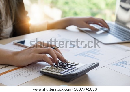 Close up Business woman using calculator and laptop for do math finance on wooden desk in office and business working background, tax, accounting, statistics and analytic research concept