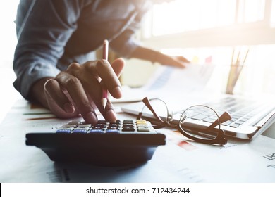 Close up of businessman or accountant hand holding pen working on calculator to calculate business data, accountancy document and laptop computer at office, business concept - Shutterstock ID 712434244