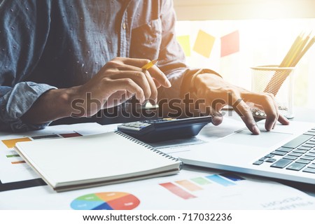 Close up of businessman or accountant hand holding pencil working on calculator to calculate financial data report, accountancy document and laptop computer at office, business concept