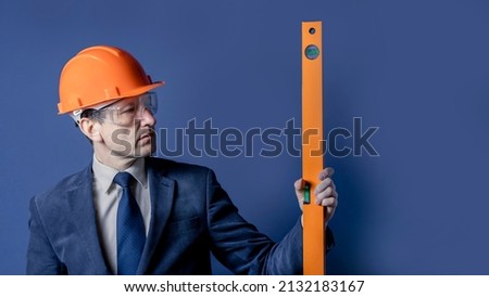 Close up of a businessman or engineer in a construction hard hat holding a measuring level in his hand.