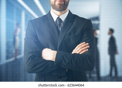 Close Up Of Businessman With Folded Arms On Blurry Office With Charts Background. Business Concept