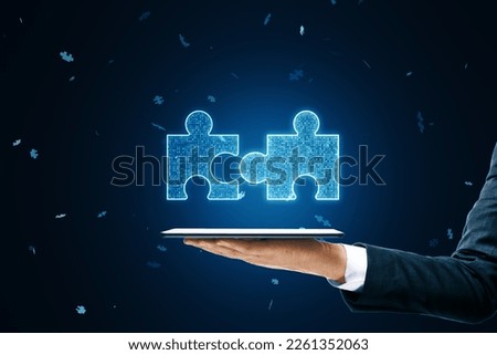 Close up of businessman hand holding mobile phone with glowing digital blue jigsaw puzzle hologram on dark blurry background. Digital solution, collaboration, partners , merge, matching concept
