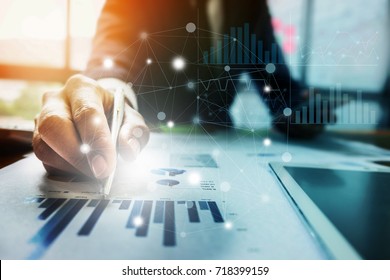 Close up Businessman hand holding pen and pointing at financial paperwork with financial network diagram. 