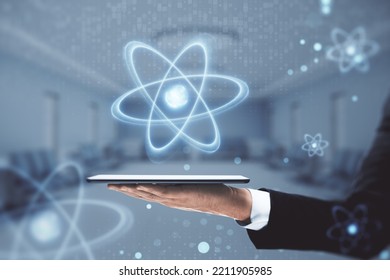 Close Up Of Businessman Hand Holding Tablet Or Smartphone With Abstract Glowing Atom Hologram On Blurry Hospital Or Clinic Interior Background. Nuclear Medicine, Energy And Medical Research Concept.