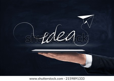 Close up of businessman hand holding tablet with creative idea airplane sketch on chalkboard background. Innovation, startup and genius concept