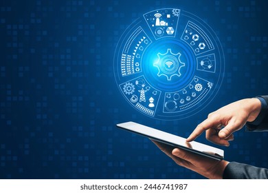 Close up of businessman hand pointing at mobile phone with round digital cogwheel and other icons hologram on blue background with mock up place. Tech support and innovation concept