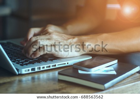 close up of businessman hand typing on smart phone with labtop in coffee shop