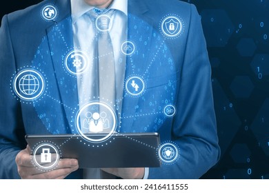 Close up of businessman hands using tablet with connected digital business interface with various icons and binary code on blurry background. Software development, global business and ai concept