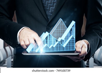 Close up of businessman hands using tablet with abstract glowing business chart hologram on interior background. Economy and sales concept - Shutterstock ID 749100739