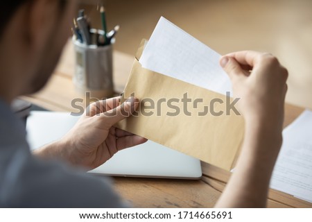 Close up businessman holding envelope with blank paper sheet, focused man looking at letter, received news, notification or invitation, working with correspondence, sitting at work desk