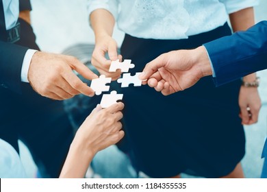 Close up at a businessman holding hands. Four puzzles come together. It represents teamwork. Must have understanding in working in the same direction in order to fully and effectively work.  