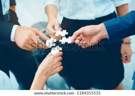 Close up at a businessman holding hands. Four puzzles come together. It represents teamwork. Must have understanding in working in the same direction in order to fully and effectively work.  