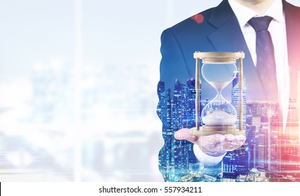 Close up of a businessman holding hourglass. Office. Night cityscape. Concept of time management. Mock up. Toned image. Double exposure 