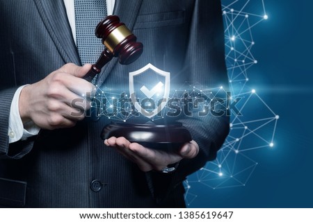 A close up of a businessman holding a juridical gavel and a protection shield with quality sign inside. The concept of law quality and protection.