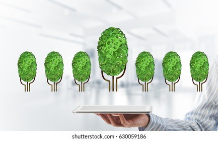 Close of businessman holding tablet pc with green tree made of gears and cogwheels. Mixed media - Shutterstock ID 630059186