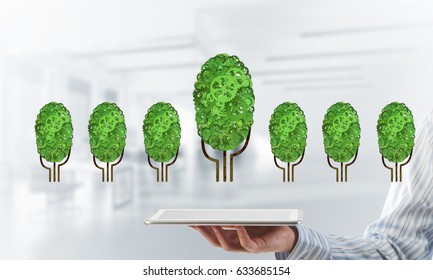 Close of businessman holding tablet pc with green tree made of gears and cogwheels. Mixed media - Shutterstock ID 633685154