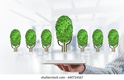 Close of businessman holding tablet pc with green tree made of gears and cogwheels. Mixed media - Shutterstock ID 640714567