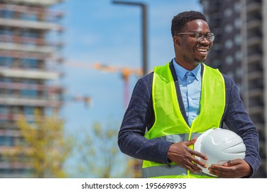 Close Up Businessman Holding White Hard Hat Builder Construction Estate. Engineer Holding Yellow Helmet For Workers Security On Background Of New Highrise Apartment Buildings