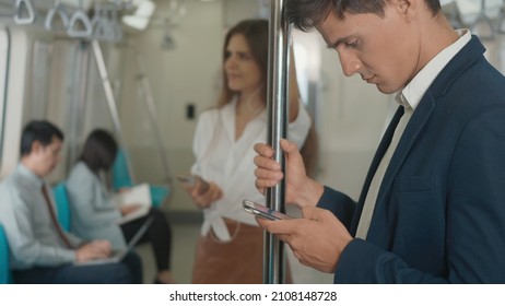 Close Up Businessman Standing On The Seat Using Modern Smartphone To Internet Checking News On Electric Train, Passenger Young Man Commuting Texting On Mobile Phone By Railway Transport