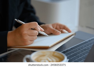 Close up businessman taking notes and using laptop at workplace