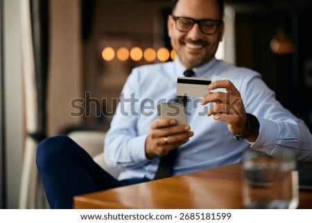 Close up of businessman using mobile app while paying online with a credit card in a cafe.