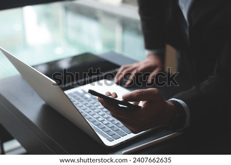 Close up of businessman using mobile phone during busy working on laptop computer at office. Business man using smartphone on mobile app, searching the information, internet networking