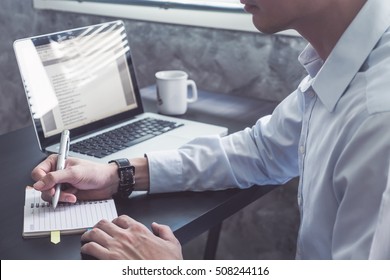 Close Up Of Businessman Writing Some Data In Notebook On The Desk.