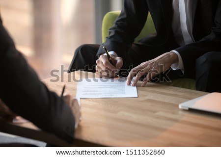 Close up businessmen signing partnership agreement, business partners making legal deal, putting signature on official paper document, taking loan or purchase property, male hands holding writing pen