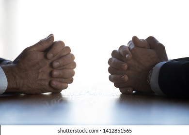 Close up of businessmen sit at table with clasped hands having dispute or discussion, serious men opponents talk negotiating at desk with arms clenched, engaged in dialogue. Rivalry concept