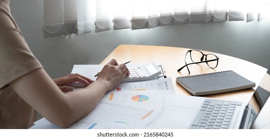 Close up of businesswoman or accountant using calculator to calculate calculate business data, working at office with paper document and laptop computer on office table, business and finance concept
