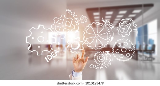 Close of businesswoman hand touching gears on screen with finger and office at background - Shutterstock ID 1010123479