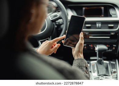 Close up of businesswoman hands is using phone while sitting behind steering wheel in own car - Powered by Shutterstock