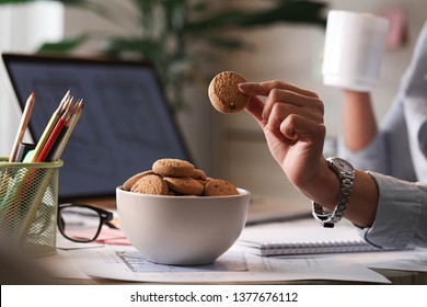 Close up of businesswoman taking cookie from a bowl while working in the office.