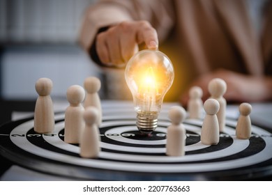 close up of businesswomen holding bulb light center point on dart board with wooden peg dolls, teamwork, competitive, success, goals, strategy, partnership, business solution concept.
