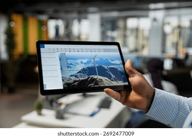 Close up of CAD engineer using tablet app in office to upgrade turbine, boosting power output, reducing carbon footprint. Worker using digital device to review windmill data to optimize clean energy