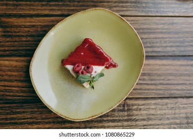 Close Up Of Cake Dessert Cheesecake With Raspberry Sauce On Plate Lying On Rustic Wooden Table In Coffee Shop Cafe Restaurant. Overhead Top View. Lifestyle Concept. Copy Space Advertisement Area