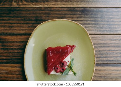 Close Up Of Cake Dessert Cheesecake With Raspberry Sauce On Plate Lying On Rustic Wooden Table In Coffee Shop Cafe Restaurant. Overhead Top View. Lifestyle Concept. Copy Space Advertisement Area