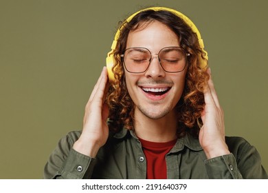 Close Up Calm Charming Fascinating Young Brunet Curly Man 20s Wears Khaki Shirt Jacket Glasses Listen Music In Headphones Have Fun Enjoy Relax Isolated On Plain Olive Green Background Studio Portrait