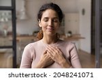 Close up of calm young Caucasian woman hold hands on heart chest feel grateful and thankful. Happy millennial female show gratitude, love and care, pray or visualize. Religion, faith concept.