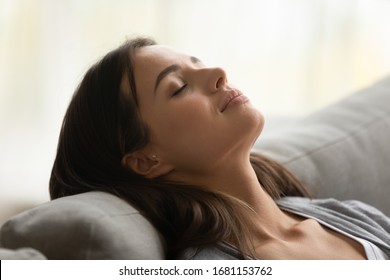 Close Up Of Calm Young Woman Relax On Couch With Eyes Closed Take Nap Sleeping At Home, Relaxed Millennial Girl Hands Over Head Rest On Sofa Breathe Fresh Air, Peace, Stress Free Concept