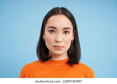 Close up of candid young asian woman, looking at camera with genuine, natural emotions, standing over blue background. - Shutterstock ID 2289740987