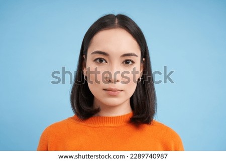Close up of candid young asian woman, looking at camera with genuine, natural emotions, standing over blue background.