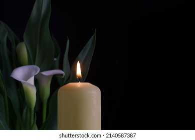 Close up of candle burning flame in the darkness and arum lilies illuminated by the candlelight alongside in a conceptual image - Shutterstock ID 2140587387