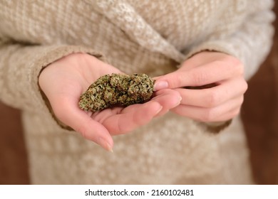 Close Up Of Cannabis Bud In Young Woman`s Hands On A Brown Background. Medical Marijuana Use Concept.