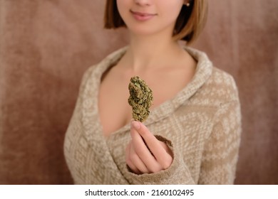 Close Up Of Cannabis Bud In Young Woman`s Hand On A Brown Background. Medical Marijuana Use Concept.