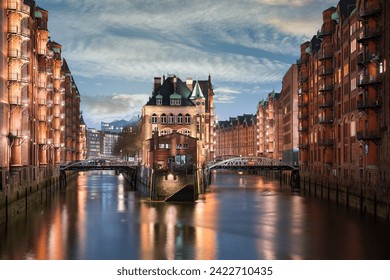 Close up capture of the famous water palace (Wasserschloss) in Hamburgs' Speicherstadt during evening with lights, cloudy sky and reflections in water - Powered by Shutterstock