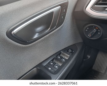 Close up of car door panel featuring window controls, door handle, and lock buttons, showcasing modern automotive interior design