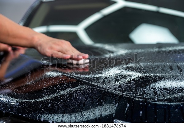 Close up car hood with blurred hand of car\
cleaner specialist wiping by cleaning clay for cleaner focus on car\
hood. Car care detailing.