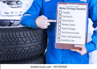 Close Up Of A Car Mechanic Leaning On A Pile Of Tires And Showing A Winter Driving Tips On The Clipboard