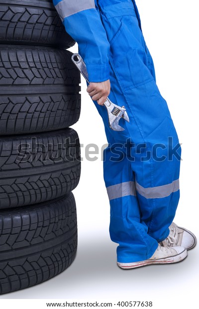 Close up\
of a car mechanic wearing uniform and leans on the tires while\
holding a wrench, isolated on white\
background
